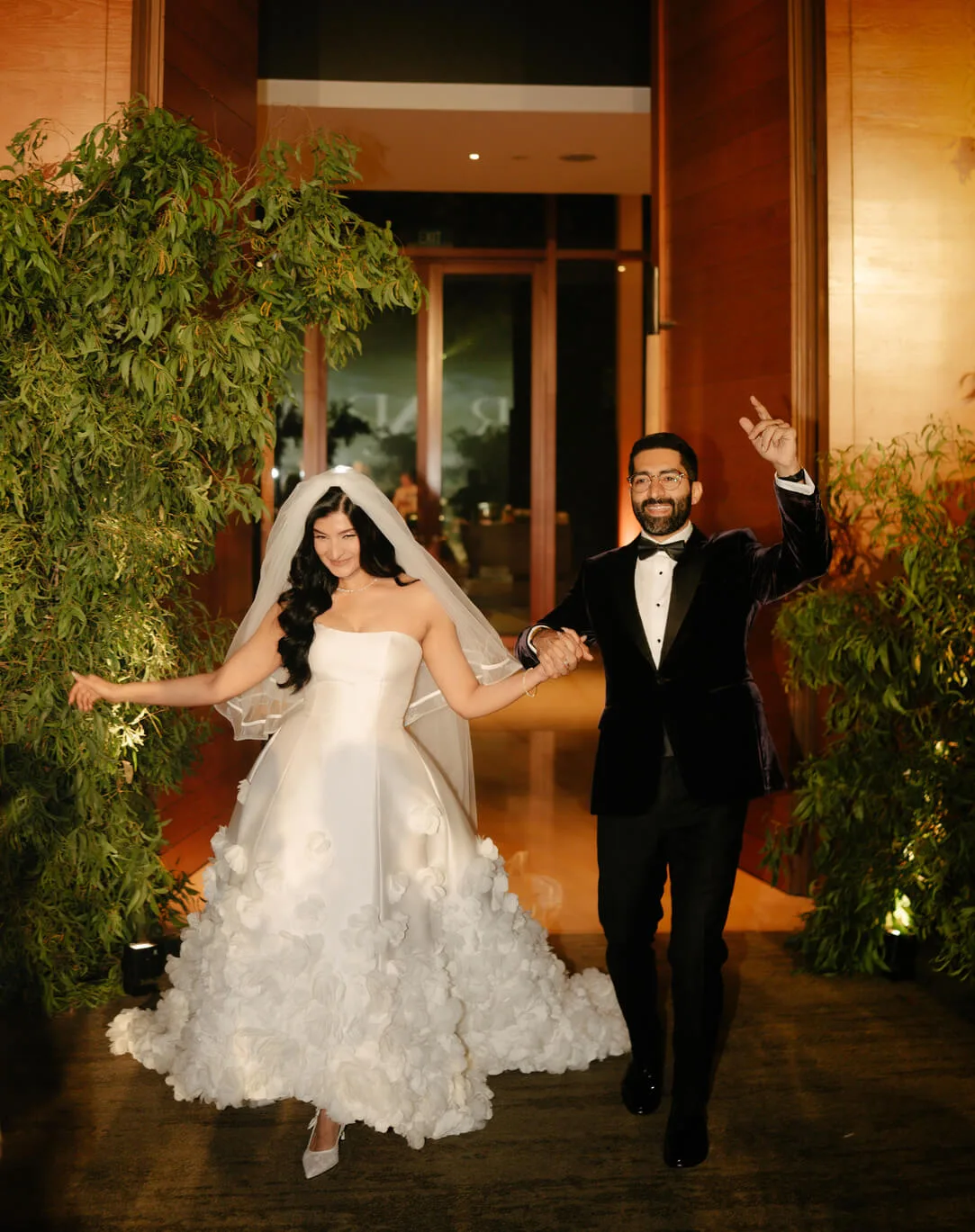 Groom in a black bespoke tuxedo by Laxmi Tailors holding hands with his bride at an evening garden reception