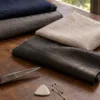 Lightweight tropical suiting fabrics in navy, grey, stone linen and charcoal mohair on a bespoke tailor's cutting table at Laxmi Tailors Jakarta